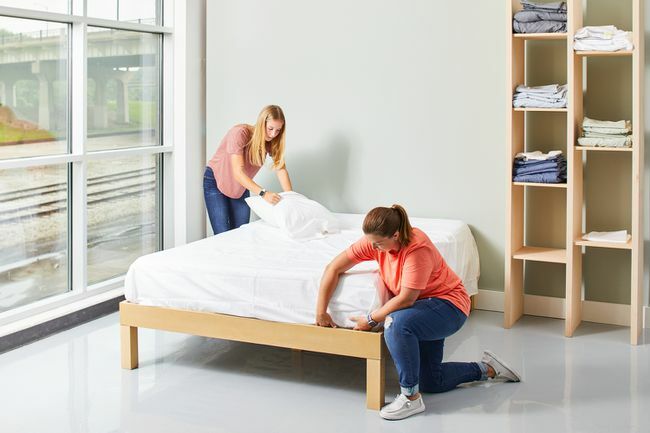 dvije žene spremaju krevet s bijelim plahtama